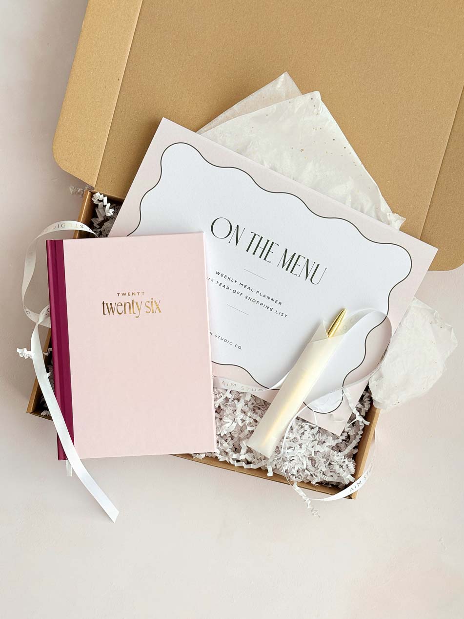 Gift box containing a pink 2026 hardback diary, weekly meal planner and pen on a light background