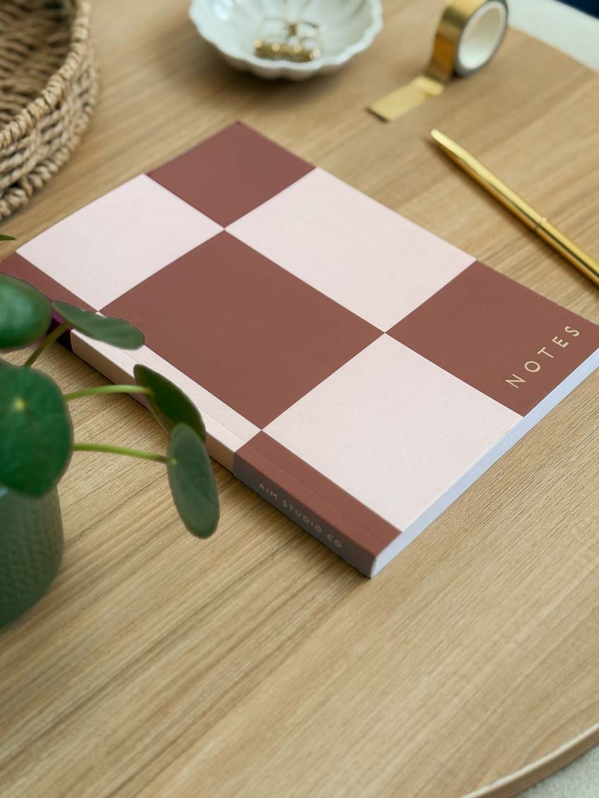 angled view of brown checkerboard notebook with gold pen on a desk