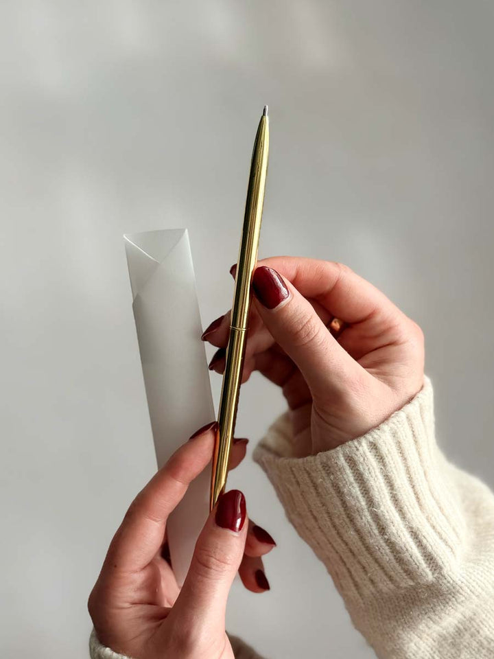 Hand holding a slim gold pen against a plain background