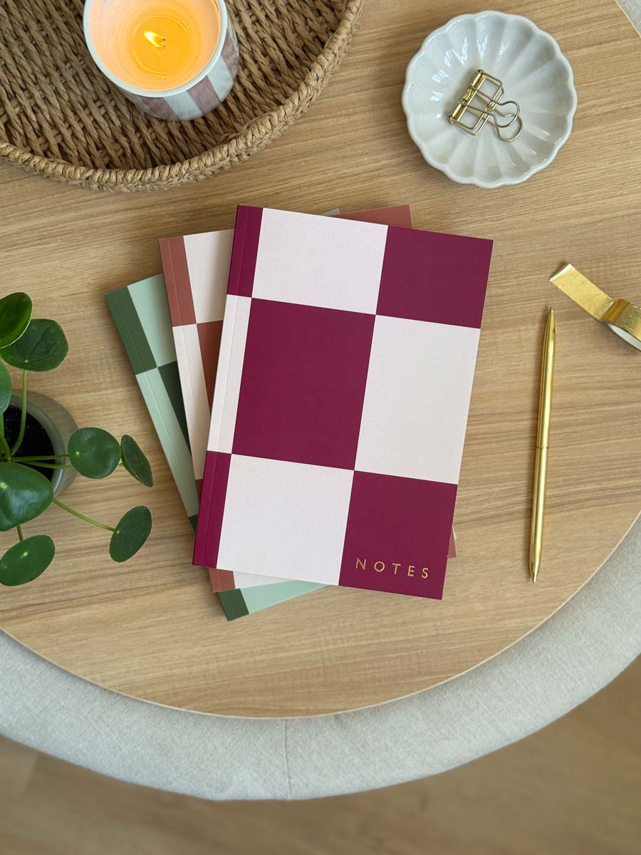 set of three a5 softcover lined notebooks with checkerboard cover design in green, pink and brown. Embossed with NOTES in gold foil in the corner of the cover