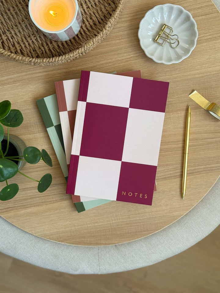 set of three a5 softcover lined notebooks with checkerboard cover design in green, pink and brown. Embossed with NOTES in gold foil in the corner of the cover