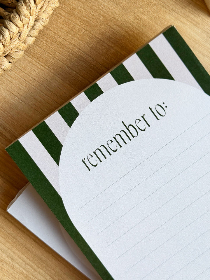A6 notepad with "remember to" in green typography and aesthetic stripe design on office desk