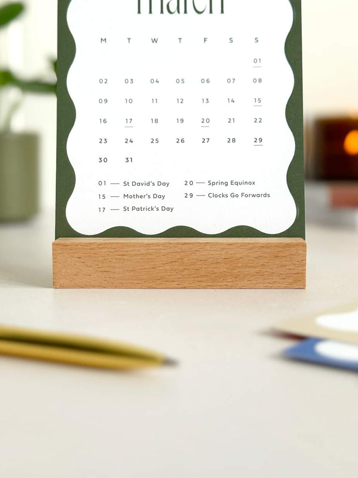 March 2026 calendar card on a stand with a blurred office desk background