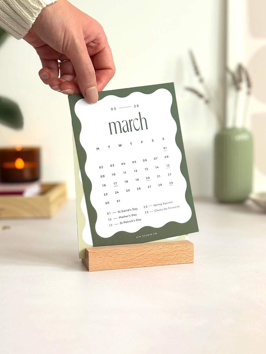 woman holding a desk calendar card showing the month of march 2026 on an office desk
