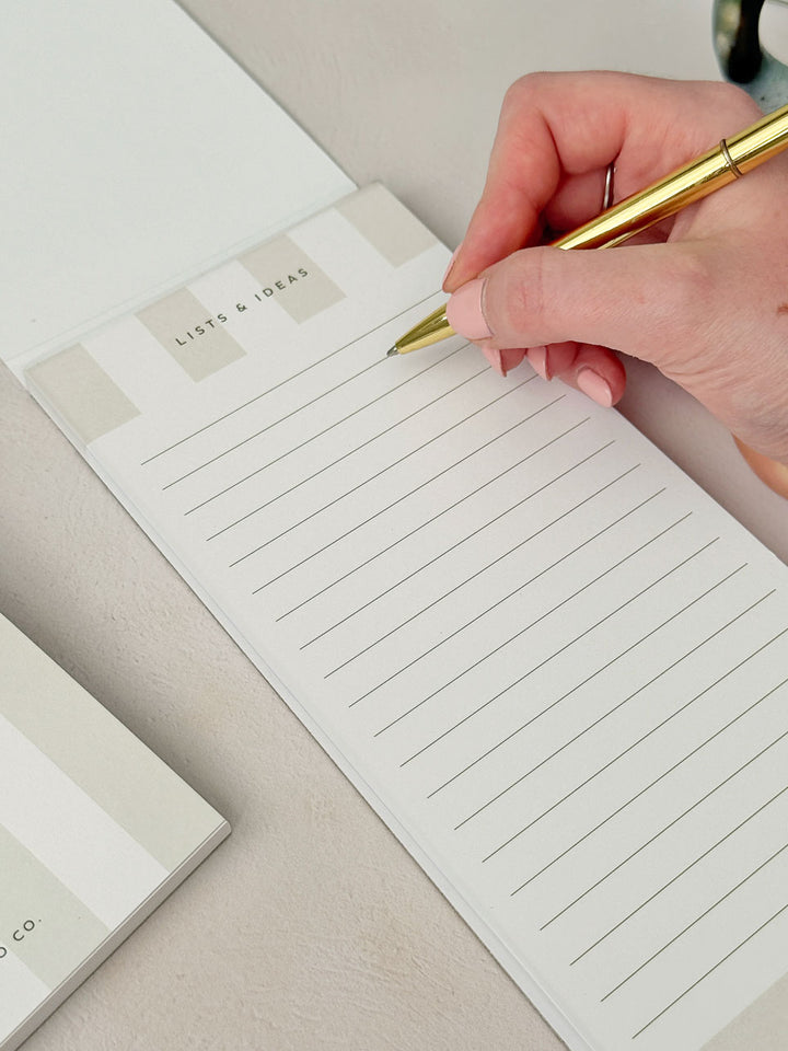 woman writing a list on a slim to do list pad with aesthetic gold pen at an office desk