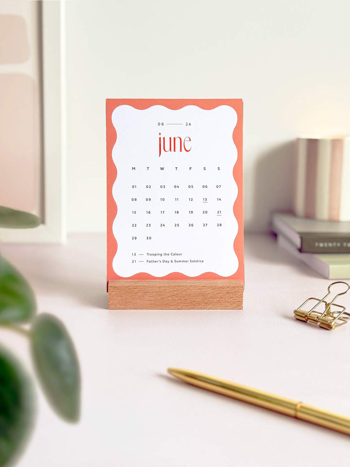 calendar card showing june 2026 in a wooden stand with stationery and desk plant