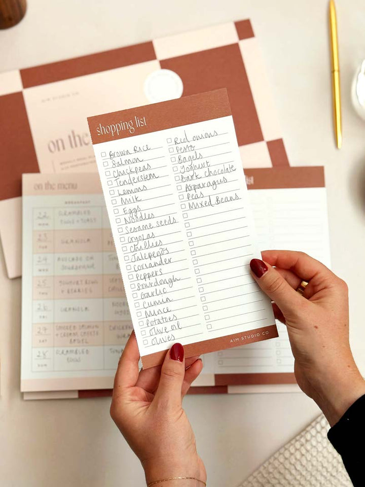 Person holding a shopping list with a checkered background