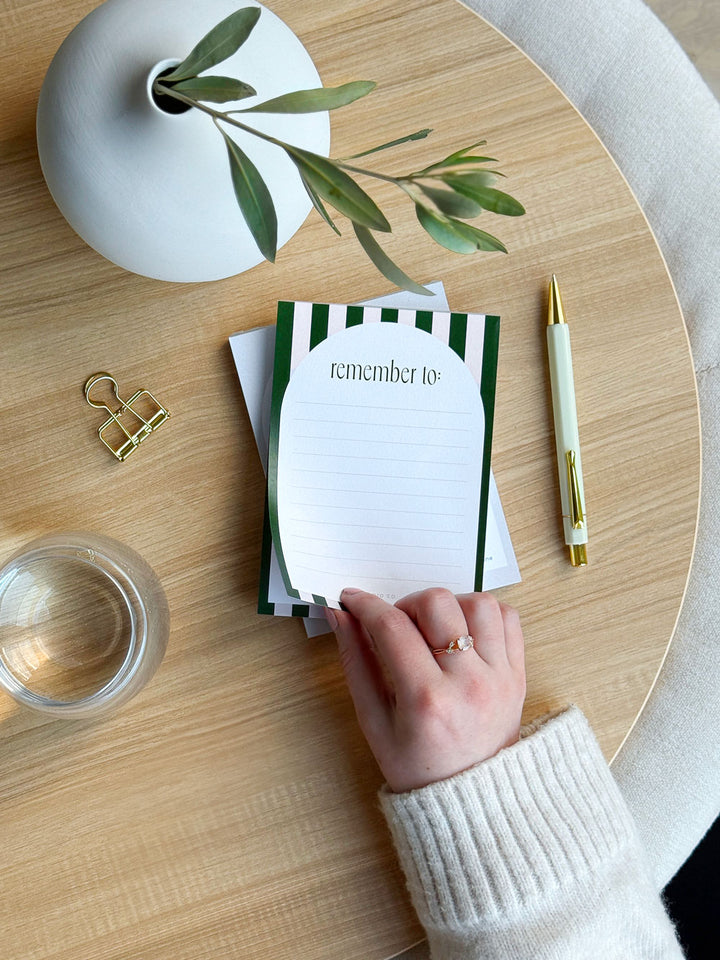 tearing off a lined page on a cute stripe notepad at an office desk surrounded by desk accessories and stationery