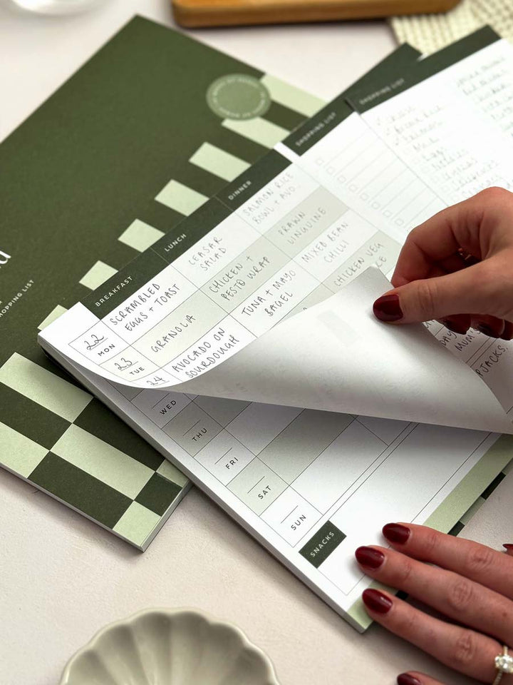 person removing tear-off notepad page with weekly food plan for breakfast, lunch and dinner.
