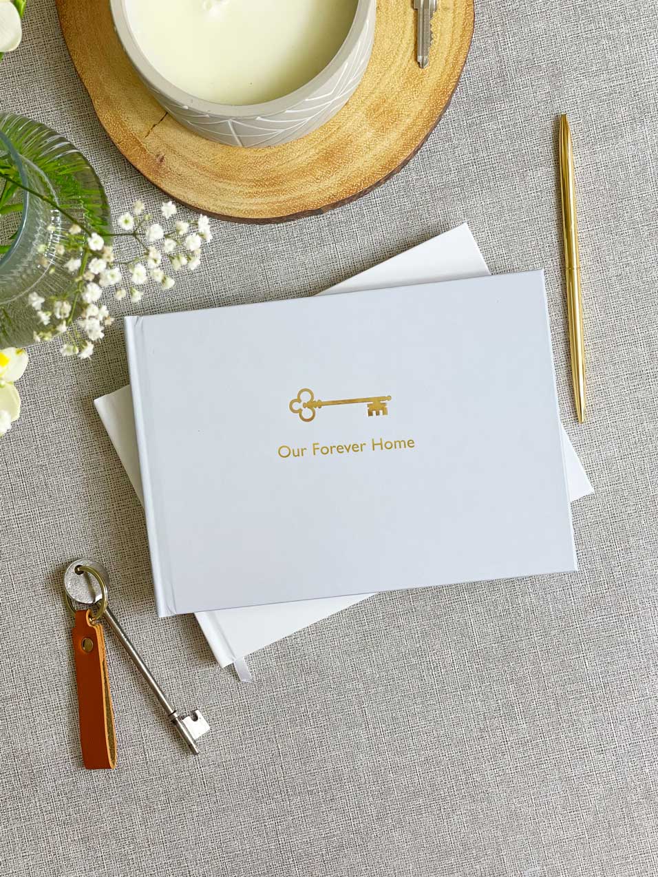 Grey hardback cover of memories scrapbook with key icon and gold foiled personalisation on the cover reading Our Forever Home