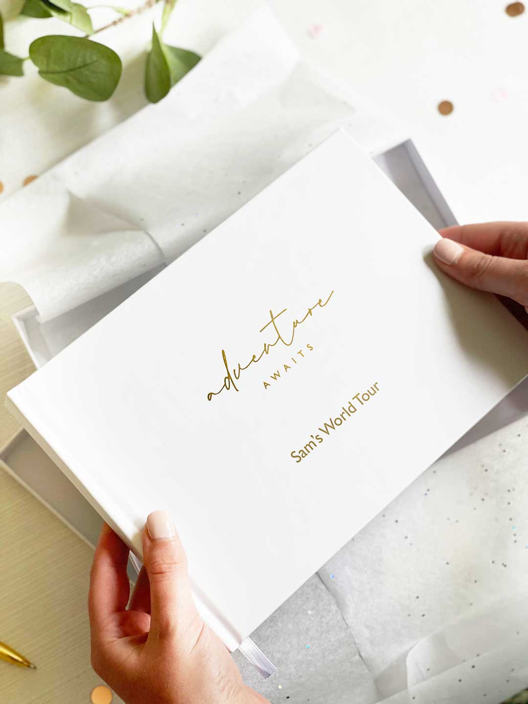 person holding an a5 landscape travel memory book with adventure awaits and a personalised name on the cover embossed in gold foil