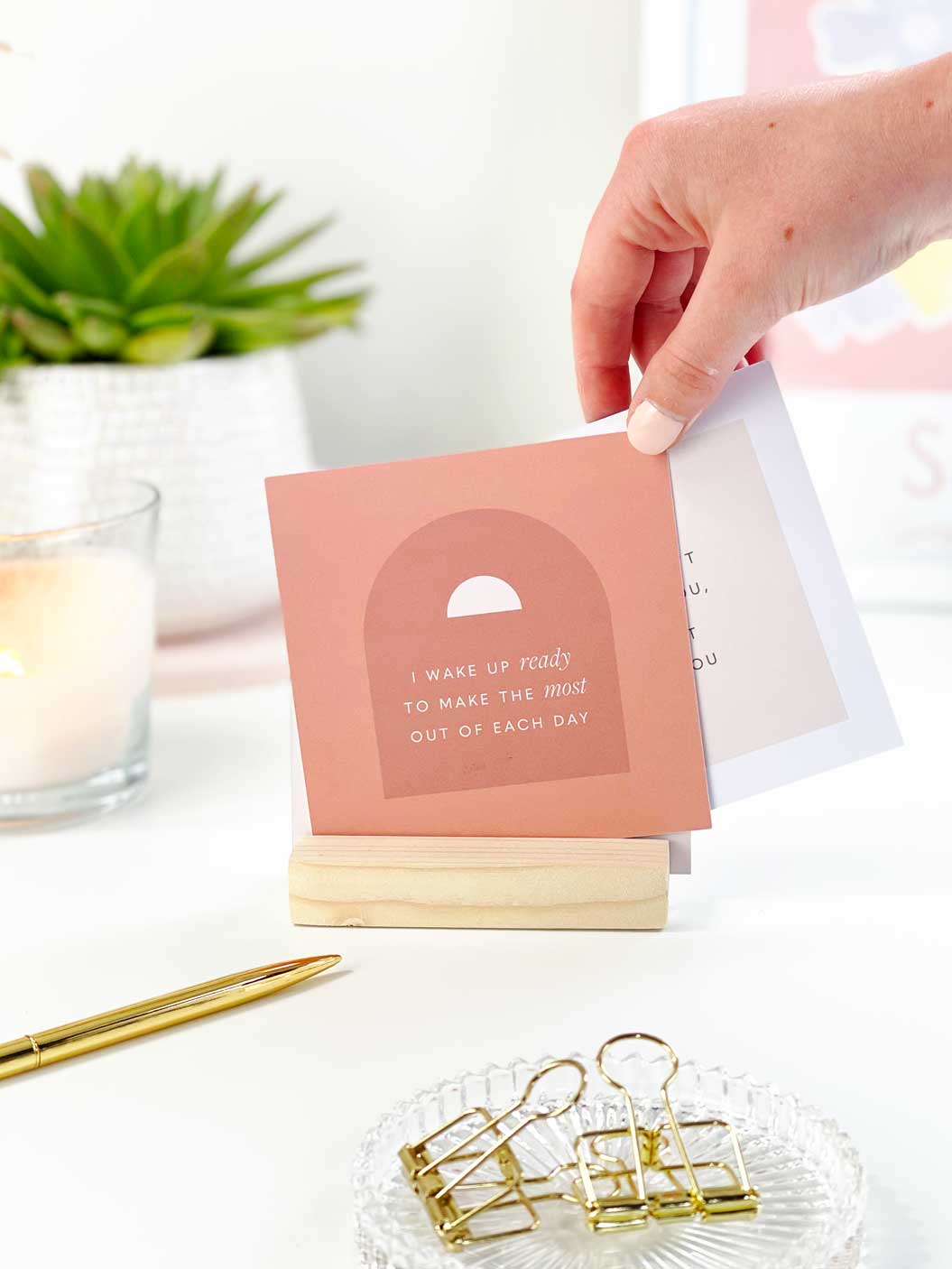 A person changing positive affirmation cards that are displayed in a wooden holder on a light office desk