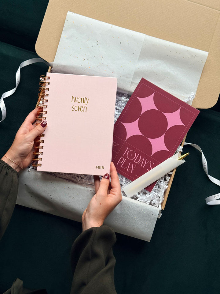 person holding a pale pink 2027 spiral diary with &