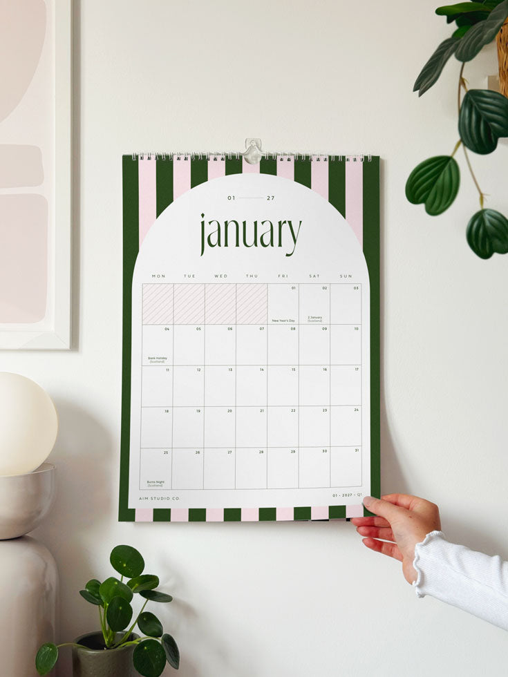 A 2027 wall calendar with a green and pink striped border shows January 2027 with monthly planner grid featuring UK bank holidays.
