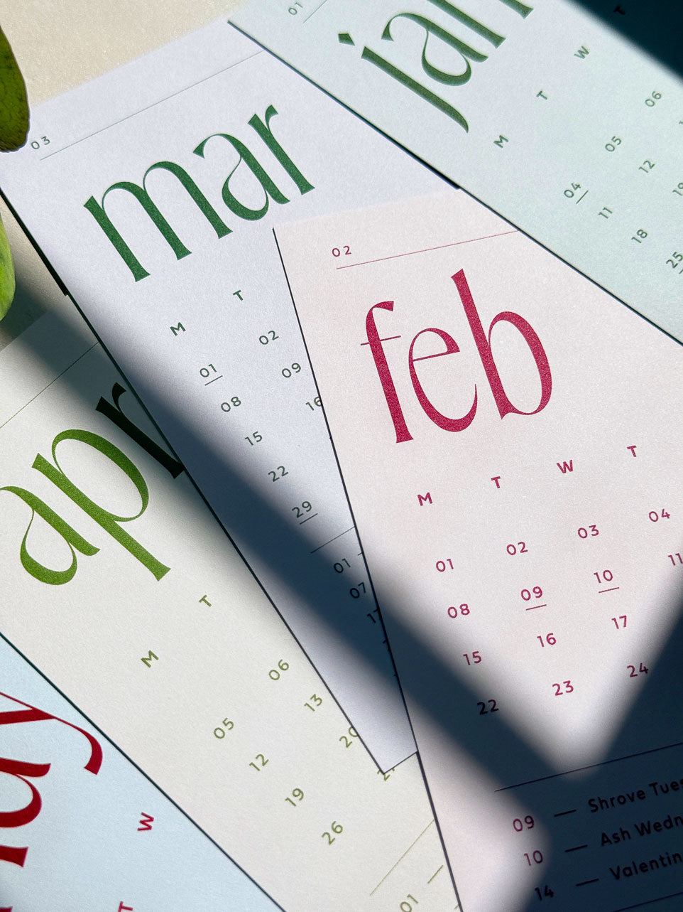 a close up of 2027 monthly calendar cards in bright sunlight with cast shadows. The detail shows uncoated paper texture and chigh quality ink printing on the minimal calendar design.