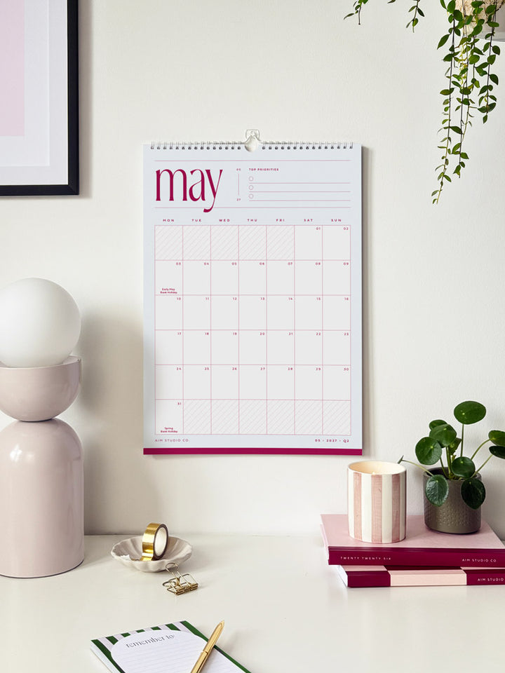 blue and pink a3 large wall planner hanging above a desk showing the month of may 2027. styled with aesthetic desk accessories.