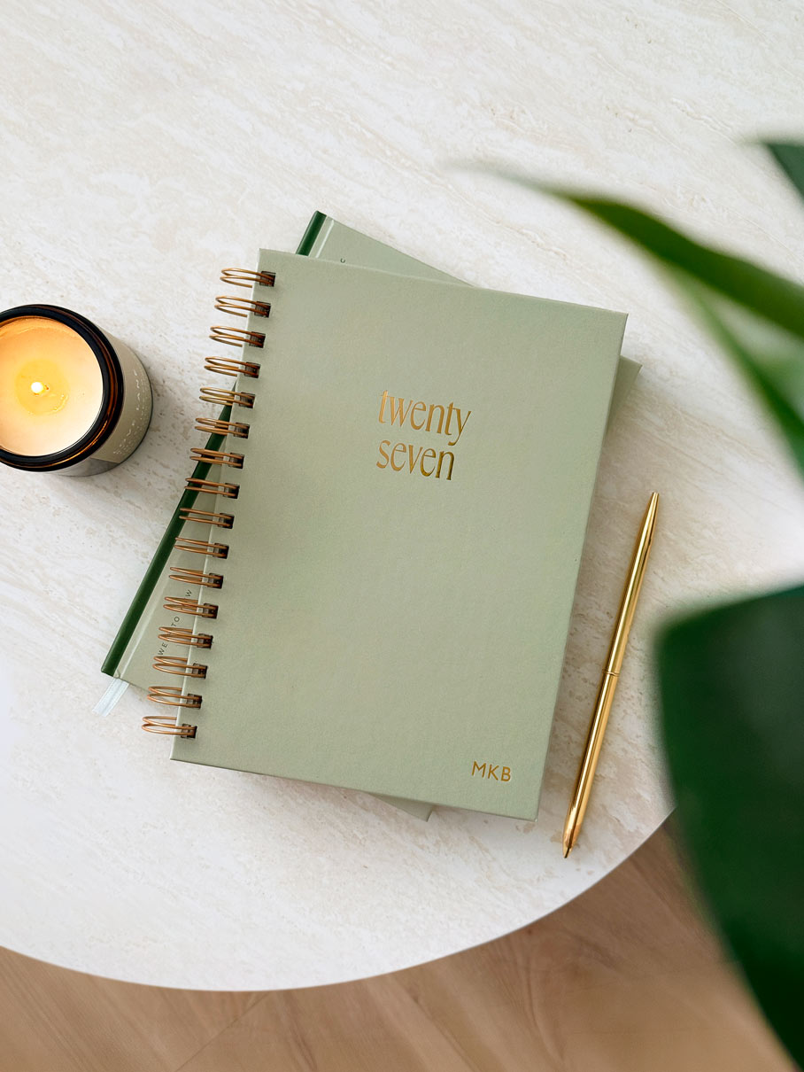 A 2027 sage green spiral-bound planner with gold foil text reading &