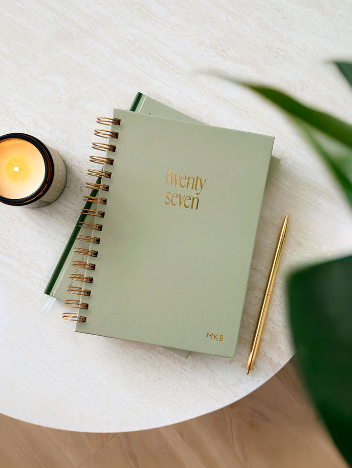 A 2027 sage green spiral-bound planner with gold foil text reading &
