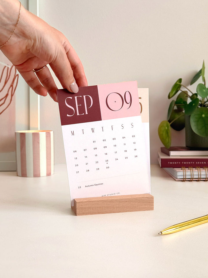changing cards of a small desk calendar dispalying the month of September 2027. The calendar card is A6 in size and features a blush pink and burgundy colour palette with minimal month to view calendar grid beneath the bold title.