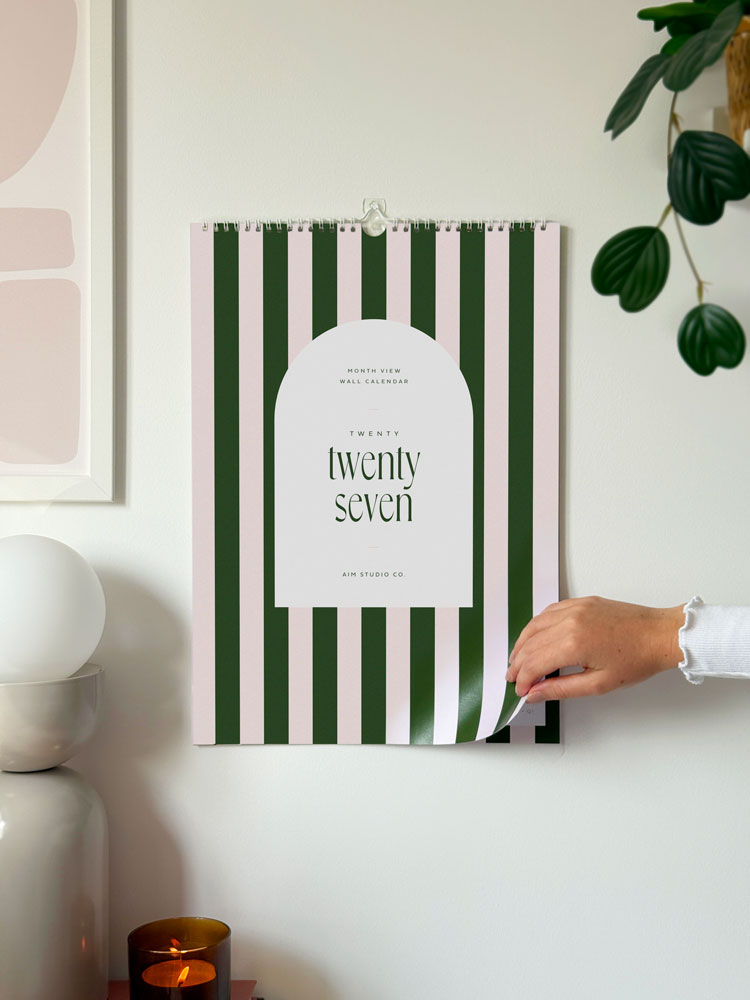 a wall hanging a3 sized calendar showing the cover of 2027 candy striped wall planner in deep green and pink, by aim studio co.