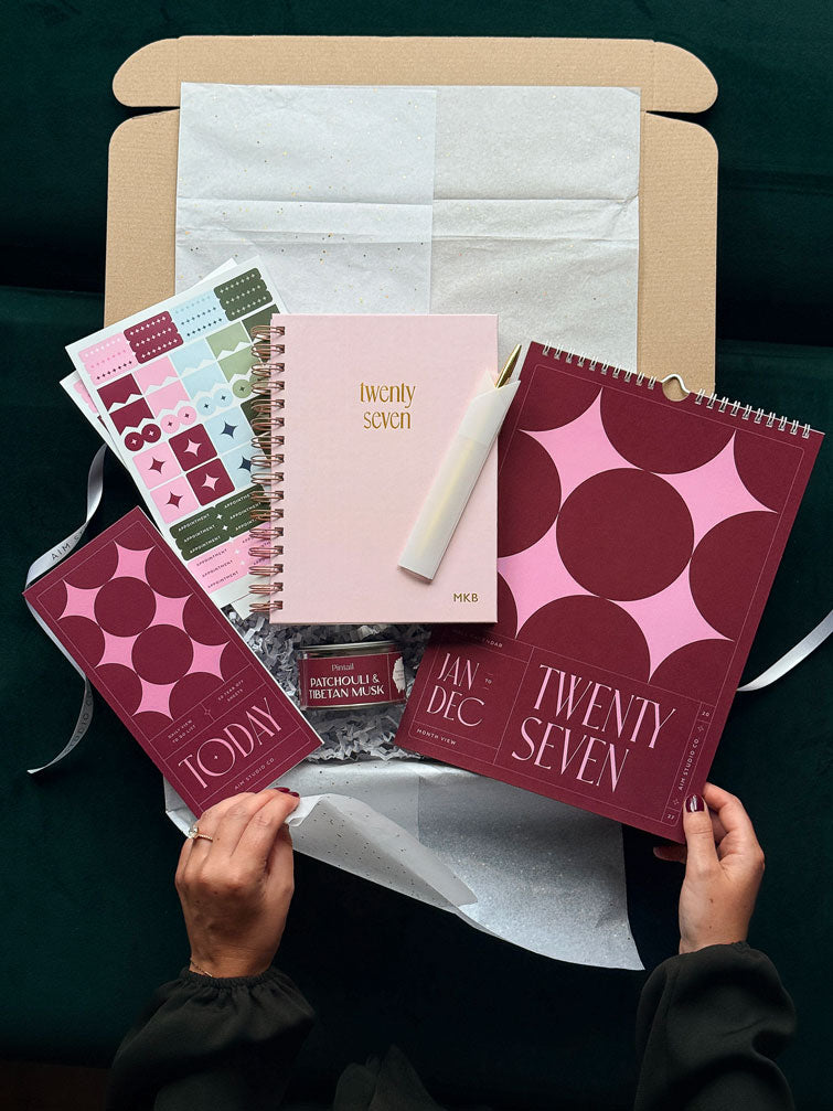 Burgundy and pink stationery gift set with a personalised 2027 spiral diary and matching desk accessories, styled on an office desk.