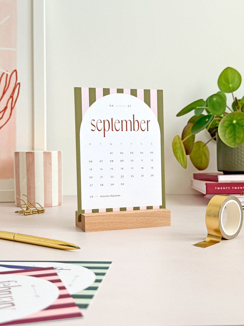 small desktop calendar with wooden stand showing the month of September 2027 with stripe design and modern serif typography.