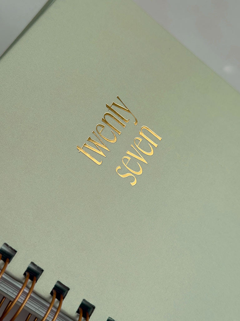 A close-up of a sage green spiral diary with &
