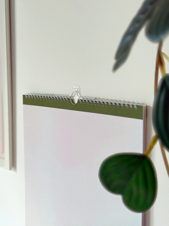 close up of white wire binding and hanging loop of 2027 minimalist a3 calendar hooked onto a wall. 