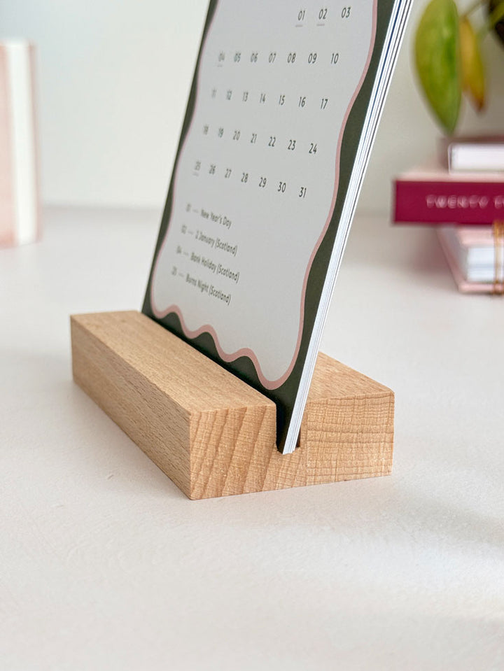 close up of monthly calendar cards held in a wooden stand on an office desk.