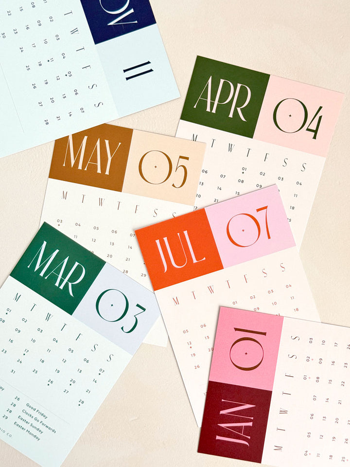 scattered a6-sized calendar cards showing various months in 2027 with bold, colourful heading and oversized aesthetic typography.