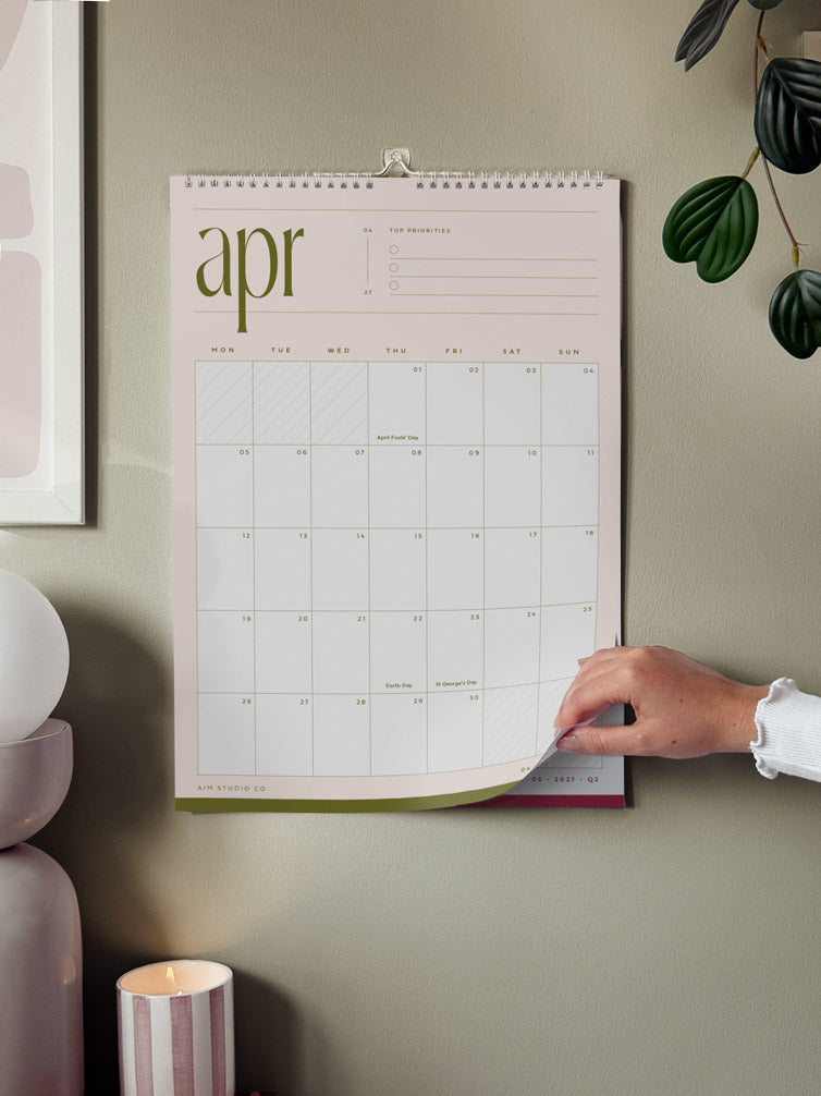 calendar with the month of april 2027 hanging on a wall showing woman turning the page to reveal the next month&