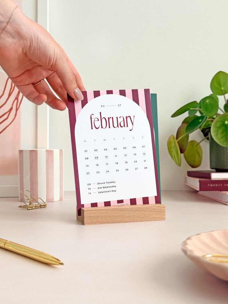 february 2027 month to view desk calendar card held in a wooden holder on office desk.