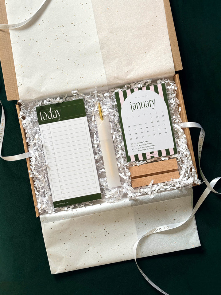 letterbox gift set with white tissue paper wrapping with a green daily time blocking notepad and pen, and 2027 candy stripe desk calendar with wooden holder. part of a desk focus stationery gift set