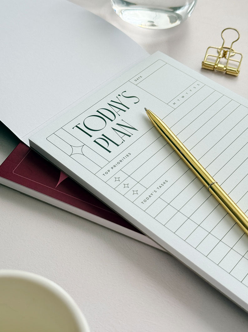 Close up of pale green undated daily planner page inside A5 notepad. A pen lies across the page and there is a bold &