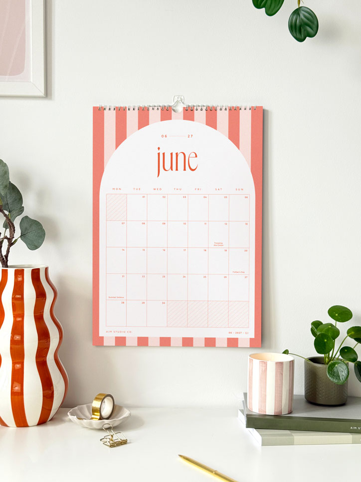 2027 hanging wall calendar above an office desk showing striped orange monthly page of june.