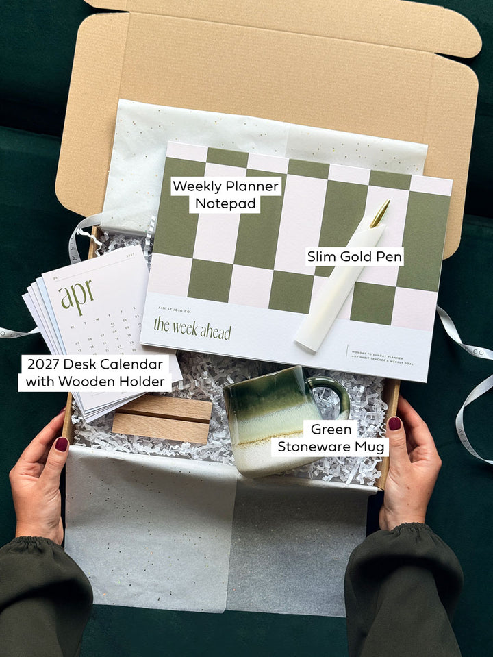 Labelled stationery items inside the Work From Home Set, a new job gift box for her: A4 weekly planner, desk calendar with wooden stand, gold pen and mug.