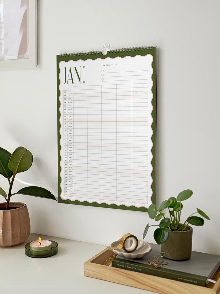 2027 family calendar showing the month of january with dark green and pink scalloped wavy border design. The planner has a vertical grid with space for 5 family members.