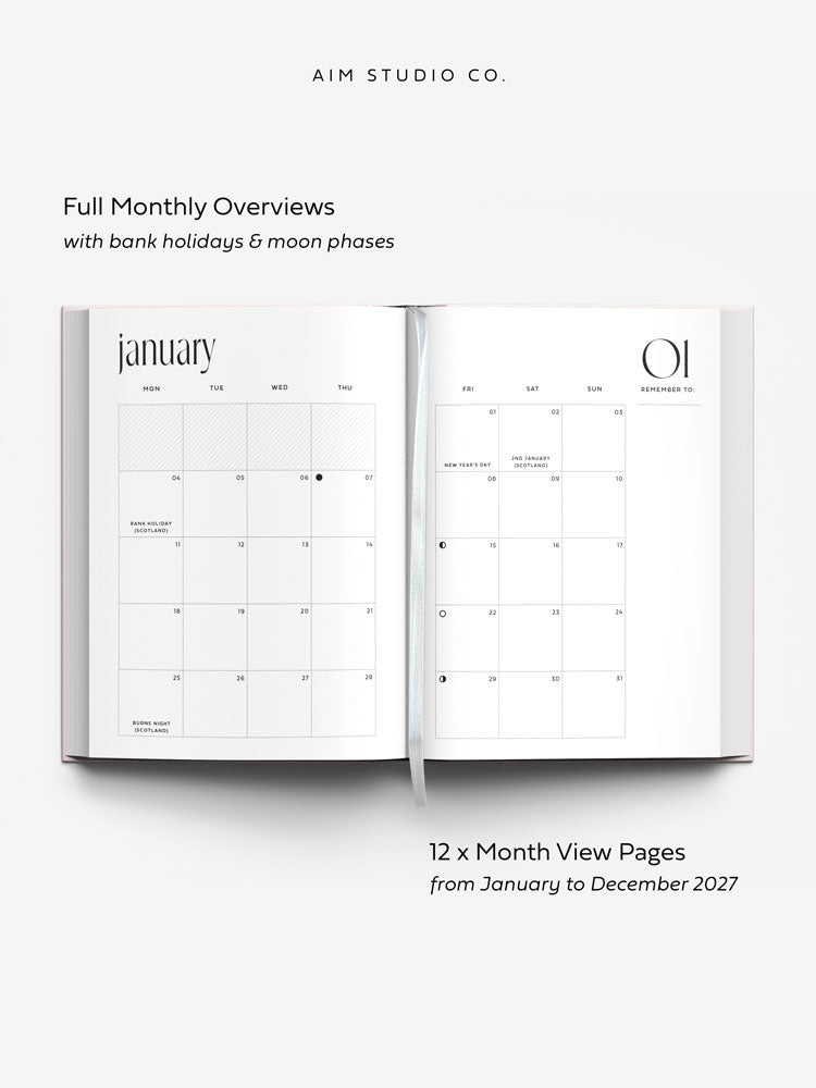 An open hardback planner showing minimalist monthly calendar pages of January 2027 with text reading &