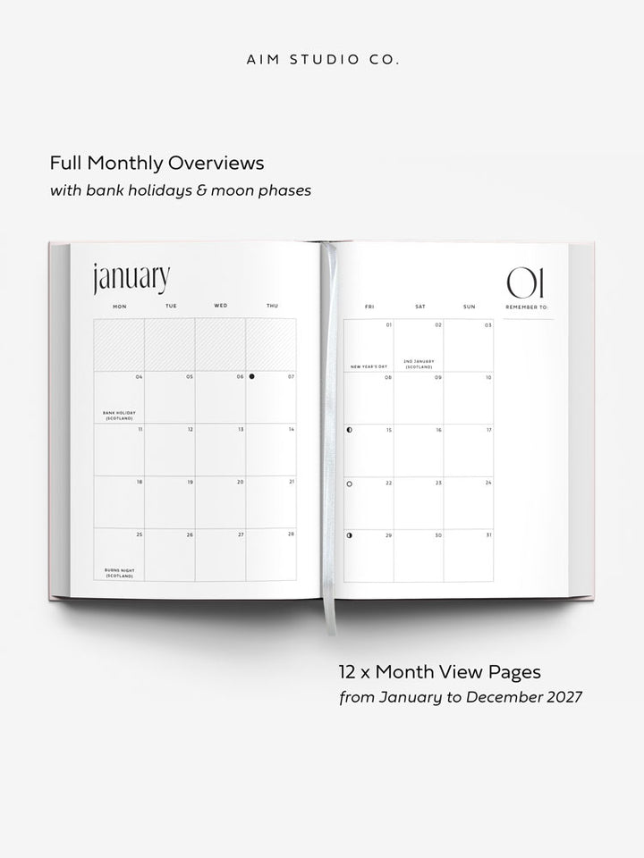 An open hardback planner showing minimalist monthly calendar pages of January 2027 with text reading &