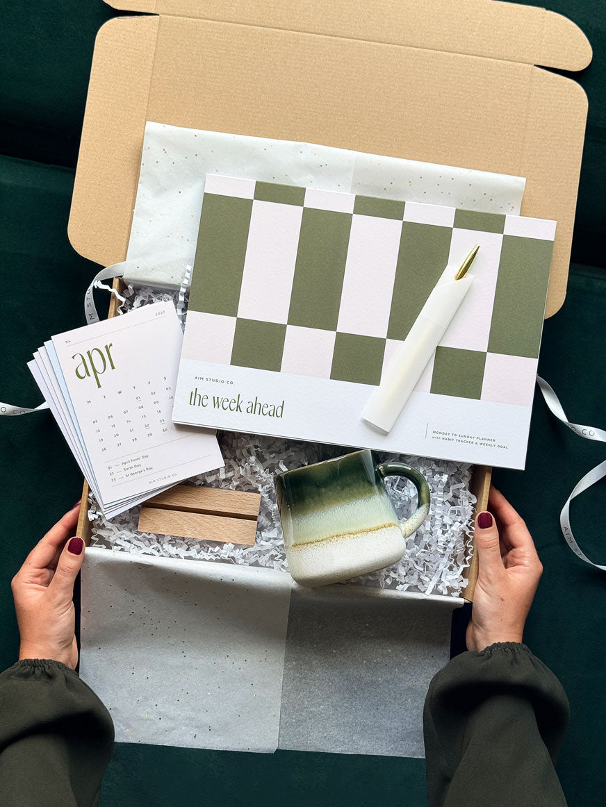 The Work From Home Set: an olive green and pink stationery bundle with an A4 weekly planner notepad, matching 2027 desk calendar, gold pen and green stoneware mug.
