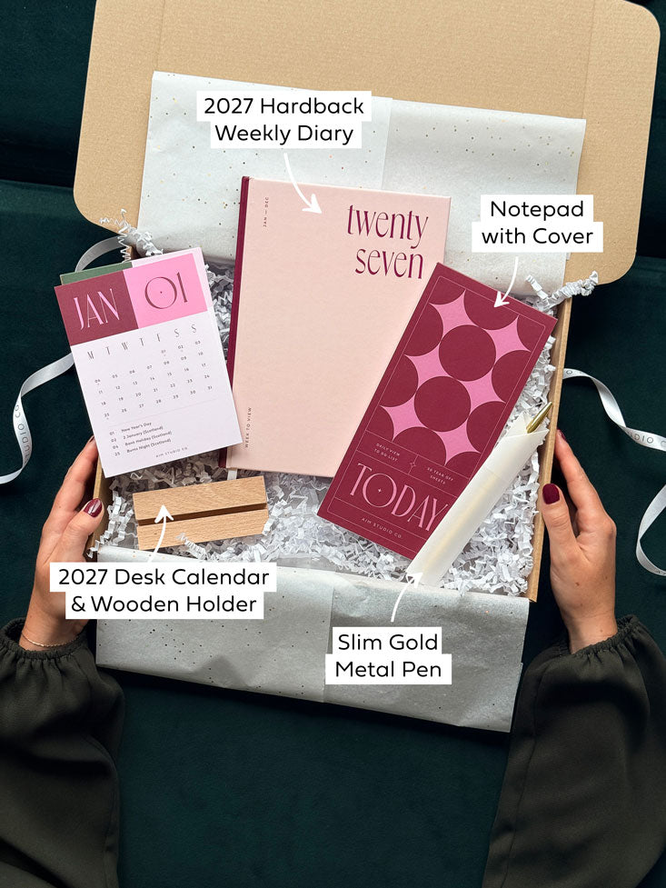 an opened stationery gift box with labels highlighting each item, including a 2027 diary planner, notepad with pen and a small desk calendar with holder.
