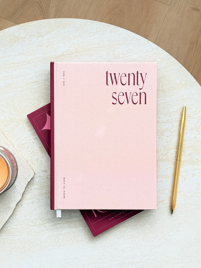 Flat lay of 2027 hardback planner by AIM Studio Co. The diary is surrounded by matching stationery including a to do list notepad and gold pen. 