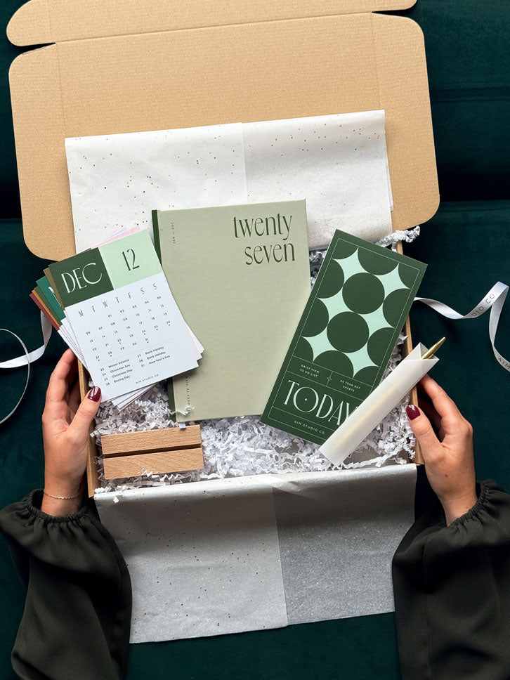 An open gift box containing a 2027 sage green diary, a &