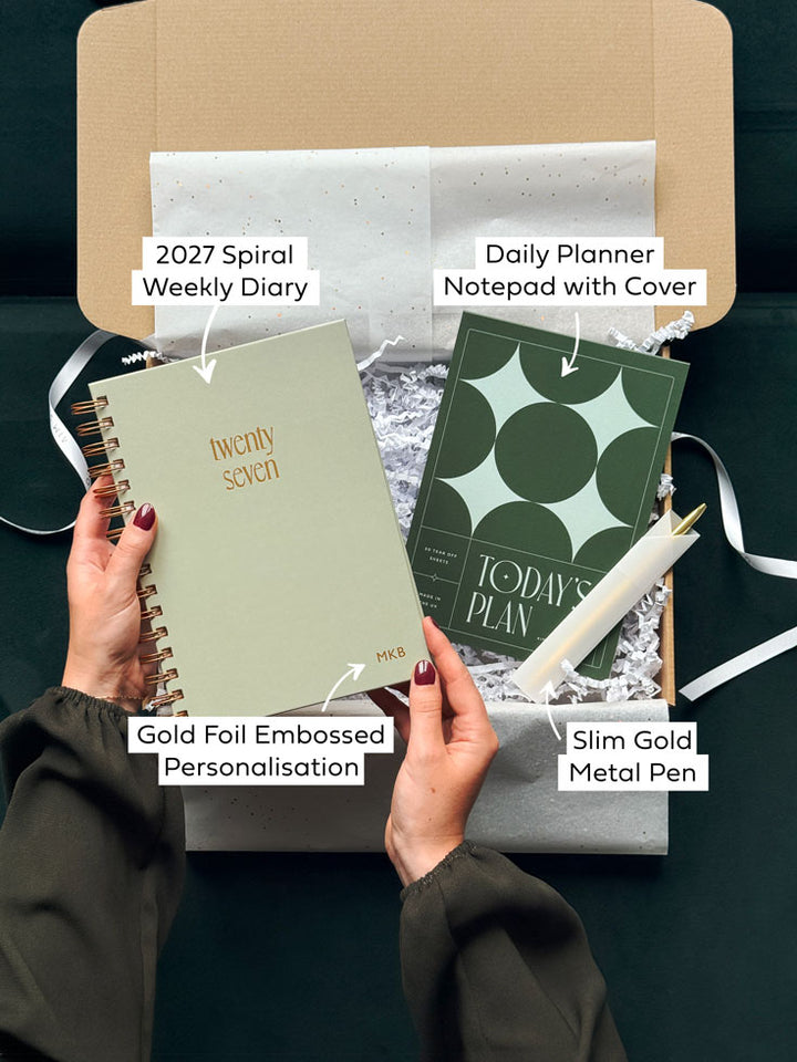 Arrows with text point to items included in a stationery gift set, highlighting a 2027 spiral diary with hardback sage green cover with gold foiled embossed personalisation, a daily planner notepad with deep green star cover and a slim gold pen.