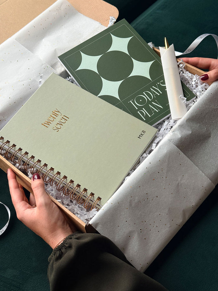 An opened Christmas gift box with sage green 2027 spiral planner embossed with gold foiled personalisation, and A5 notepad with &