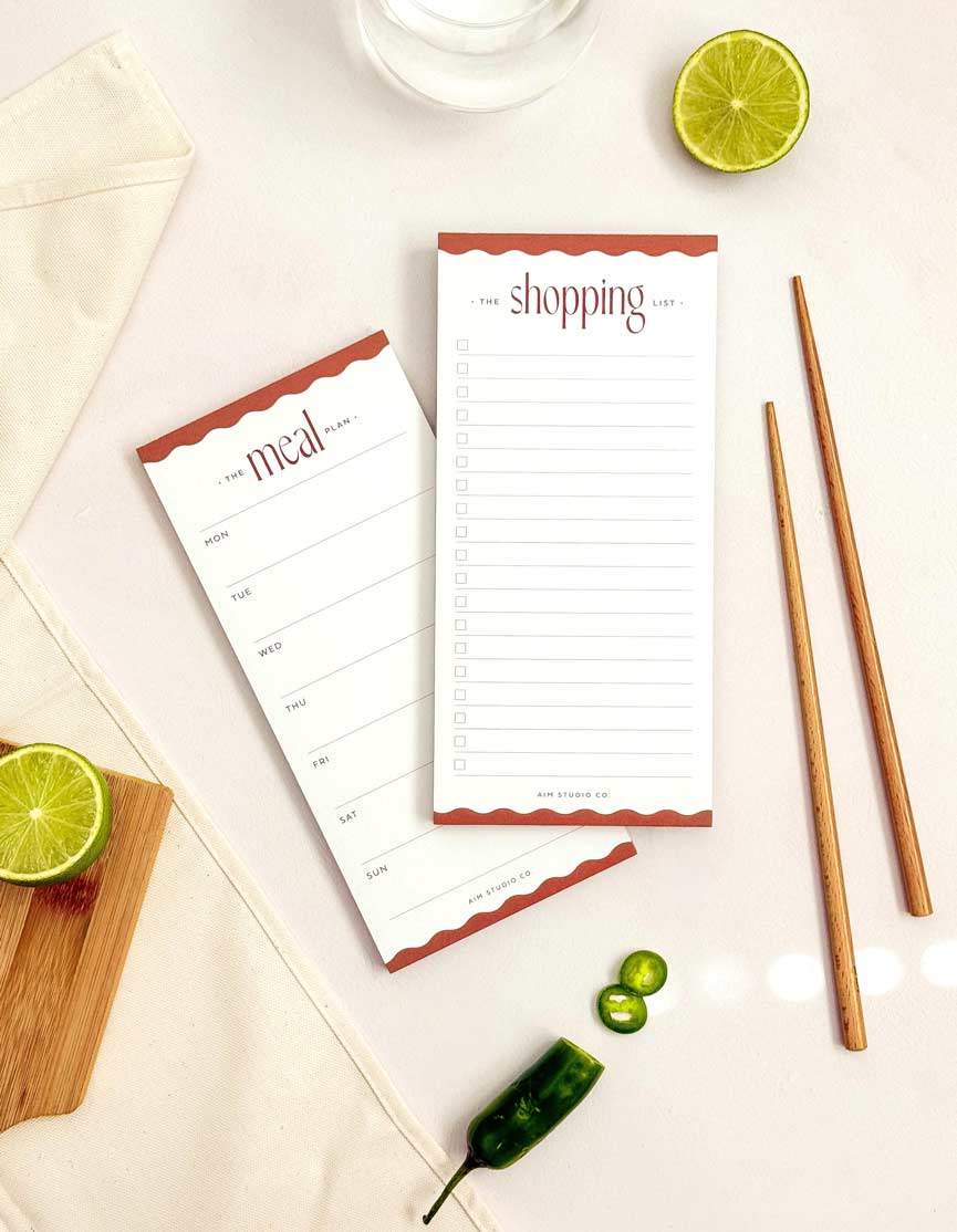 Two notepads with meal and shopping lists on a table with lime, jalapeño, and chopsticks.
