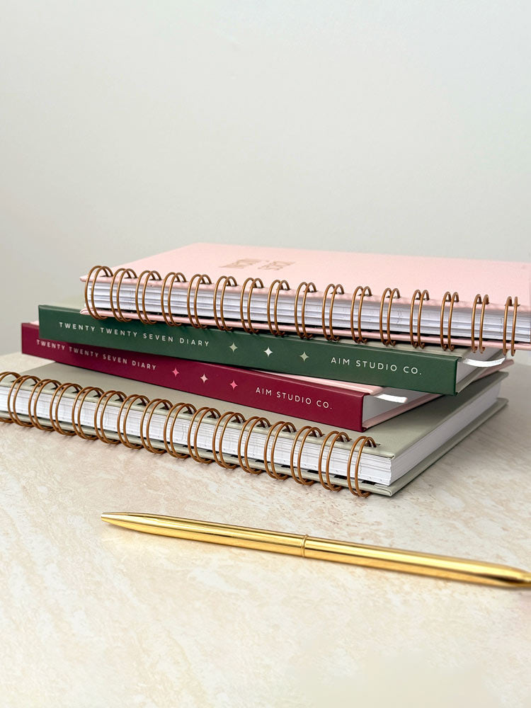 A stack of 4 2027 diary options available from AIM Studio Co. Showing pink and sage green coves in hardback and spiral ring bound planner formats.