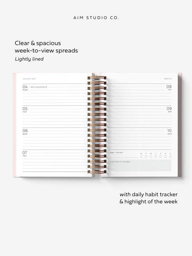 flay lay of 2027 A5 weekly planner pages showing lined daily sections with UK bank holidays and a daily habit tracker. The diary has metallic gold spiral binding.