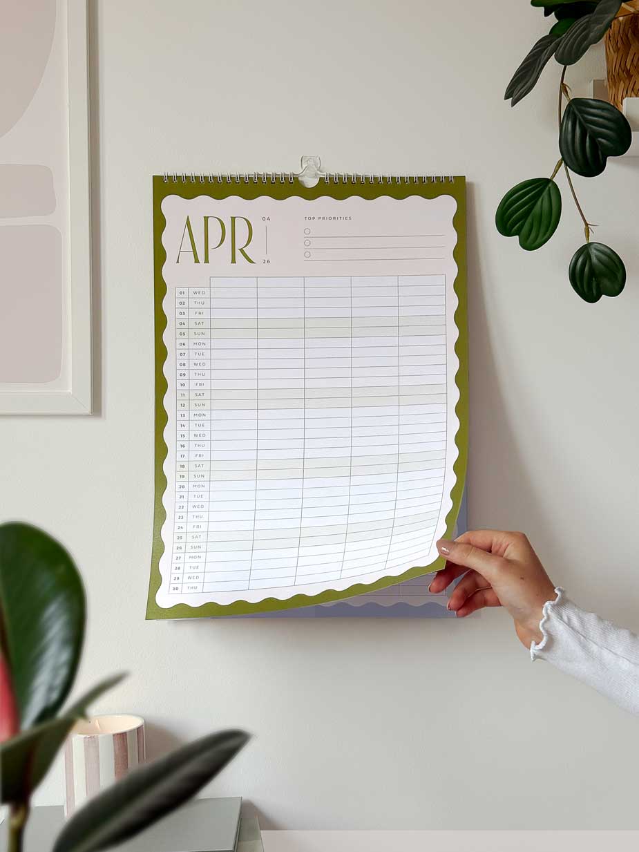 woman turning monthly calendar page on large hanging family wall planner 