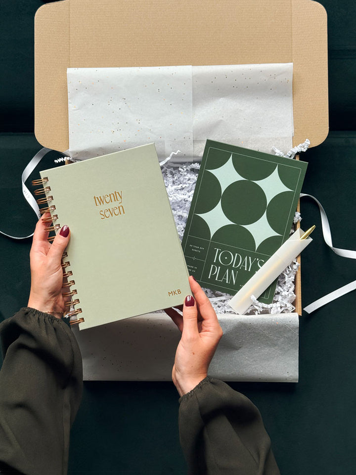 hands holding a sage green spiral bound 2027 diary with gold foiled &